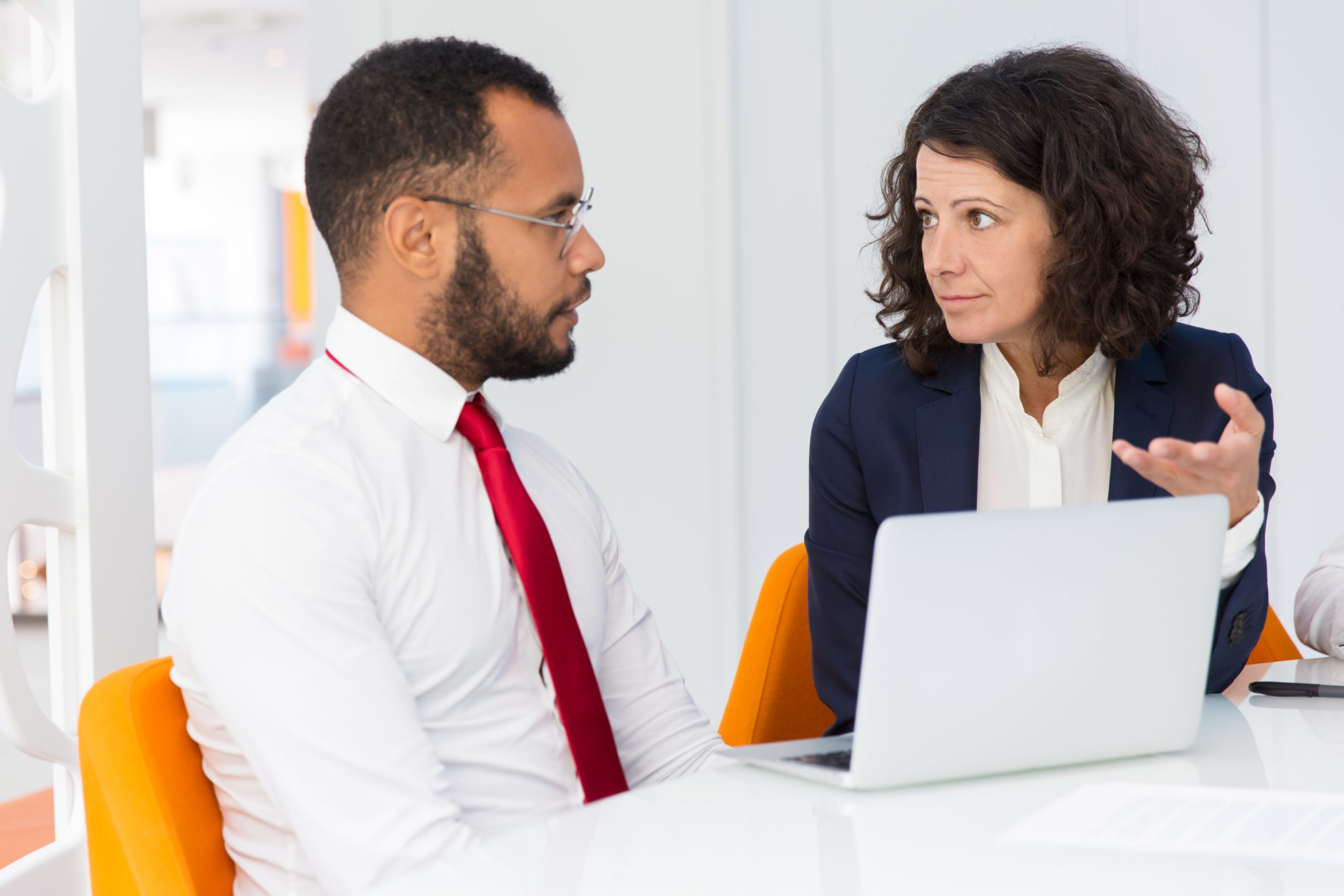 Mentor explaining project specific to intern. Business man and woman sitting at conference table with laptop, talking and gesturing. Consulting or mentorship concept